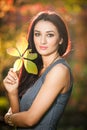 Beautiful woman in gray posing in autumnal park. Young brunette woman holding a leaf and spending time in autumn Royalty Free Stock Photo