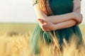 Beautiful woman in green dress walking in field and touches ears of wheat with hand at sunset light, girl enjoying summer nature Royalty Free Stock Photo