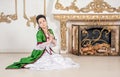 Beautiful woman in green rococo style medieval dress sitting on the floor near fireplace and praying Royalty Free Stock Photo
