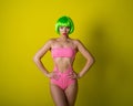 Beautiful woman in a green short wig and pink bikini posing on a yellow background. Portrait of a girl with sensual red Royalty Free Stock Photo