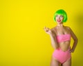 Beautiful woman in a green short wig and pink bikini posing on a yellow background. Portrait of a girl with sensual red Royalty Free Stock Photo