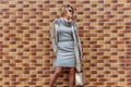 A beautiful woman in a grey dress posing against a brick wall