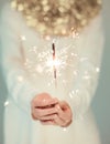 Beautiful woman hands holding sparkler lights, cozy, bright winter sweater with golden christmas garland