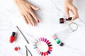 Beautiful woman hands painting nails with red nail polish on marble table with manicure set on it, top view Royalty Free Stock Photo
