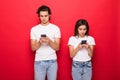 Beautiful woman and handsome man typing with smart phones back to back each other over red background Royalty Free Stock Photo