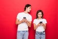 Beautiful woman and handsome man typing with smart phones back to back each other over red background Royalty Free Stock Photo