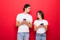 Beautiful woman and handsome man typing with smart phones back to back each other over red background Royalty Free Stock Photo