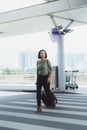 Beautiful woman happily walking along pedestrian strip with suitcase and airport on background