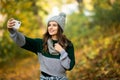 Beautiful young woman in hat, scarf and jacket in autumn takes a selfie on her phone in autumn park Royalty Free Stock Photo