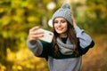 Beautiful young woman in hat, scarf and jacket in autumn takes a selfie on her phone in autumn park Royalty Free Stock Photo