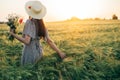 Beautiful woman in hat with wildflowers enjoying sunset in barley field. Atmospheric tranquil moment, rustic slow life. Stylish Royalty Free Stock Photo