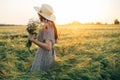 Beautiful woman in hat with wildflowers enjoying sunset in barley field. Atmospheric tranquil moment, rustic slow life. Stylish Royalty Free Stock Photo