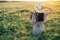 Beautiful woman in hat with wildflowers enjoying sunset in barley field. Atmospheric tranquil moment, rustic slow life. Stylish Royalty Free Stock Photo