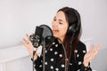 Beautiful woman in headphones sings a song near a microphone in a recording studio. Place for text or advertising