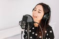 Beautiful woman in headphones sings a song near a microphone in a recording studio. Place for text or advertising