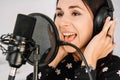 Beautiful woman in headphones sings a song near a microphone in a recording studio. Place for text or advertising