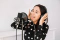 Beautiful woman in headphones sings a song near a microphone in a recording studio. Place for text or advertising Royalty Free Stock Photo