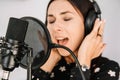 Beautiful woman in headphones sings a song near a microphone in a recording studio. Place for text or advertising