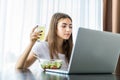 Young beautiful woman in her kitchen during her breakfast and using her laptop Royalty Free Stock Photo