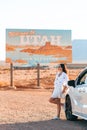 Beautiful woman on her trip by the car. Welcome to Utah road sign. Large welcome sign greets travels in Monument Valley