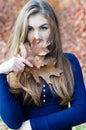 Beautiful woman hiding face behind autumn brown leaf
