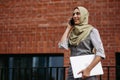 Beautiful woman in hijab standing on city street. Muslim businesswoman with laptop making call. Iran, Afganistan female