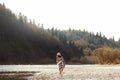 beautiful woman hipster walking on river beach in mountains,wearing hat and poncho, boho travel concept, space for text Royalty Free Stock Photo