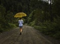 Beautiful woman hold yellow umbrella and walks on a country road under rain Royalty Free Stock Photo