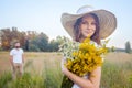 Beautiful woman holding bouquet of yellow flowers and looking at camera with her boyfriend on background. Royalty Free Stock Photo