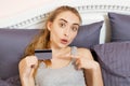 Beautiful woman holding a credit card and pointing her finger. Girl holding a bank card while sitting on bed in room Royalty Free Stock Photo