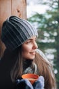 Beautiful  woman holding and drinking a cup of coffee or cocoa in gloves sitting home by the window. Blurred winter snow tree back Royalty Free Stock Photo