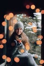 Beautiful  woman holding and drinking a cup of coffee or cocoa in gloves sitting home by the window. Blurred winter snow tree back Royalty Free Stock Photo