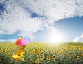 Beautiful woman holding multicolored umbrella in sunflower field and cloud sky