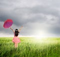 Beautiful woman holding red umbrella in green grass field and raincloud