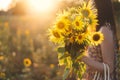 Beautiful woman holding sunflowers bouquet close up in warm sunset light in summer meadow. Tranquil atmospheric moment in