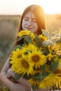 Beautiful woman holding sunflowers in evening meadow. Tranquil atmospheric moment in countryside. Stylish young female in floral