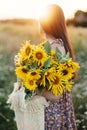 Beautiful woman holding sunflowers in summer evening meadow. Tranquil atmospheric moment in countryside. Stylish young female in