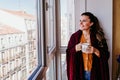 beautiful woman at home by the window, enjoying a cup of tea. lifestyle indoors, autumn season