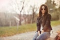 Beautiful woman in jacket and jeans sitting in a park