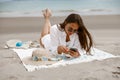 Beautiful woman in sunglasses lie on beach towel near sea and using phone during vacation Royalty Free Stock Photo