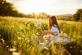 a beautiful woman in a light dress sits in a field of daisies at sunset holding a hat in her hands Royalty Free Stock Photo