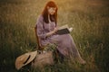 Beautiful woman in linen dress reading book sitting on chair in summer meadow sunset. Slow life Royalty Free Stock Photo