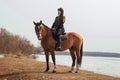 A beautiful woman with long and black hair in a historical hussar costume stands near a river with a horse Royalty Free Stock Photo