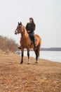 A beautiful woman with long and black hair in a historical hussar costume stands near a river with a horse Royalty Free Stock Photo