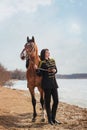 A beautiful woman with long and black hair in a historical hussar costume stands near a river with a horse Royalty Free Stock Photo