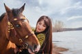 A beautiful woman with long and black hair in a historical hussar costume stands near a river with a horse Royalty Free Stock Photo