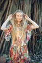 Beautiful woman with long blond hair poses on the background of trees. Portrait of a young long-haired girl