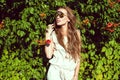 Beautiful woman with long chestnut hair wearing trendy round mirrored sunglasses standing at the Virginia creeper hedge