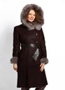 Beautiful woman with long curly red hair in black sheepskin coat with fur-trimmed hood and wide leather belt on white