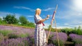 Beautiful smiling woman in long dress painting picture on easel of lavender field